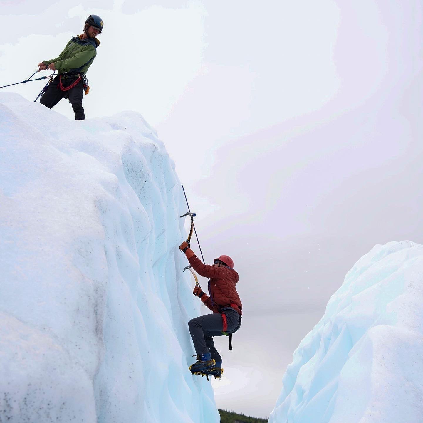 glacier guide uses rope to assist ice climber in glacier ice