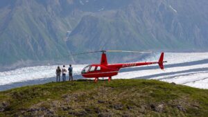 three people viewing glacier from nearby ridge with red helicopter